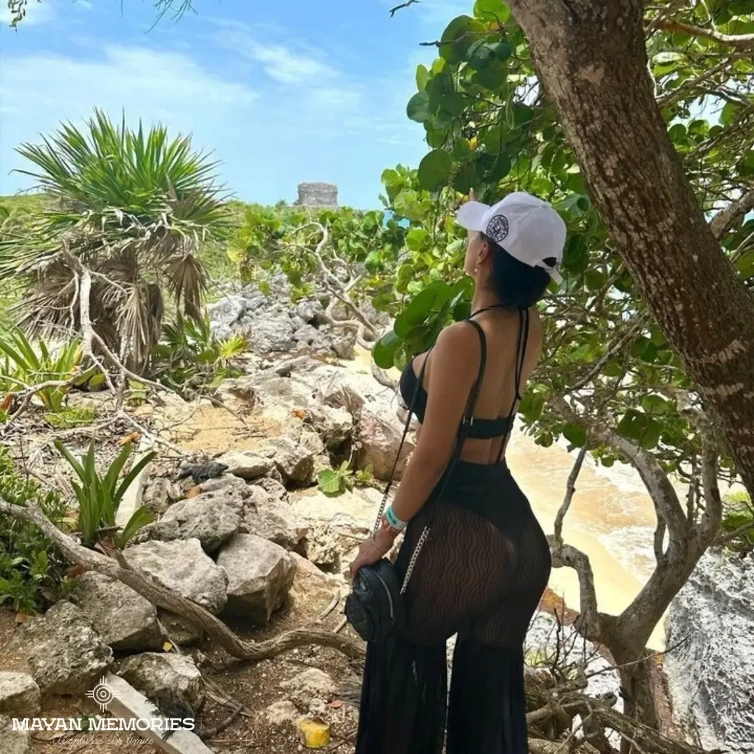 Woman in a cap looking at the Tulum ruins among the trees