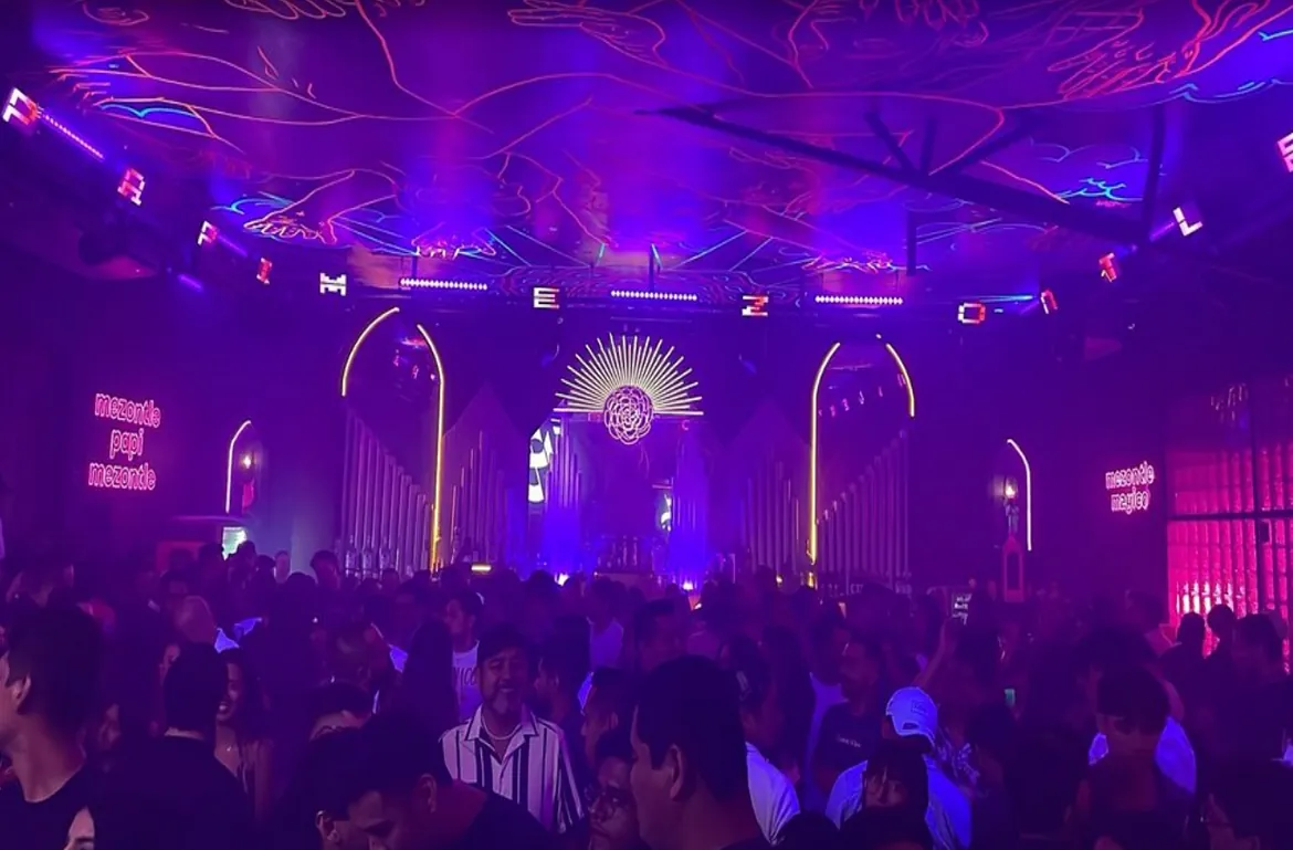 Packed dance floor under purple lights and lit arches at Mezontle
