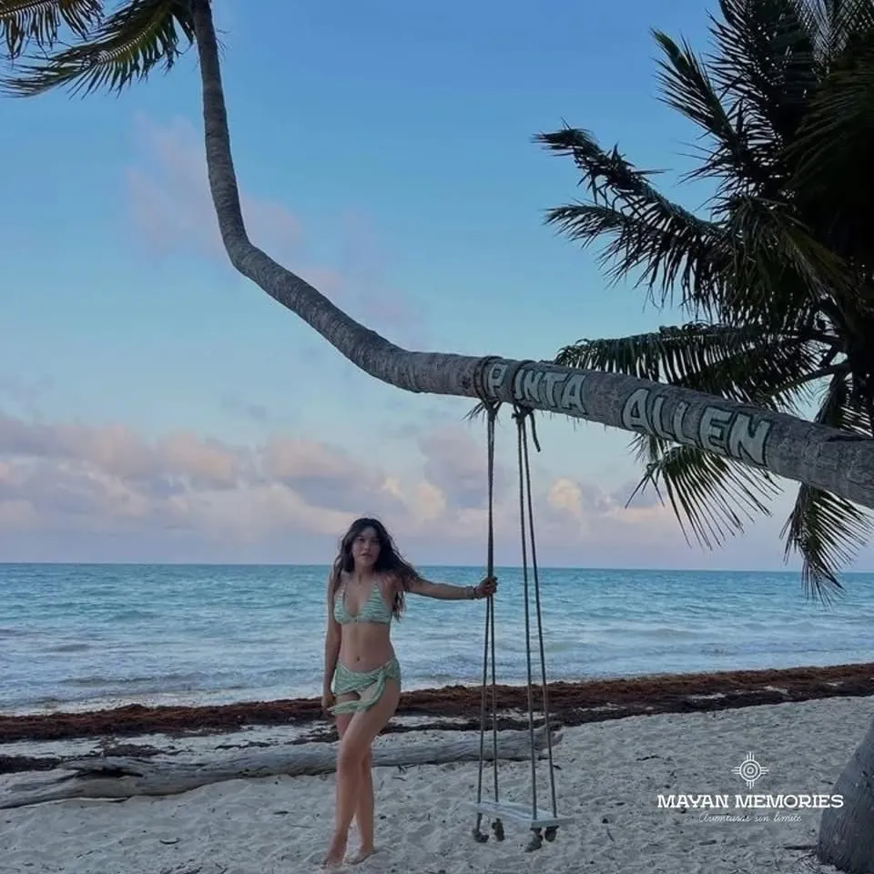 Woman on a swing hanging from a palm tree on the beach