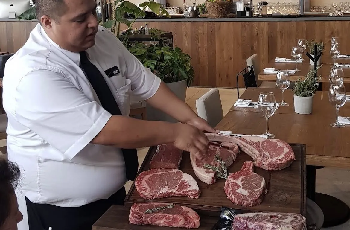 Waiter presenting raw cuts of beef at the table