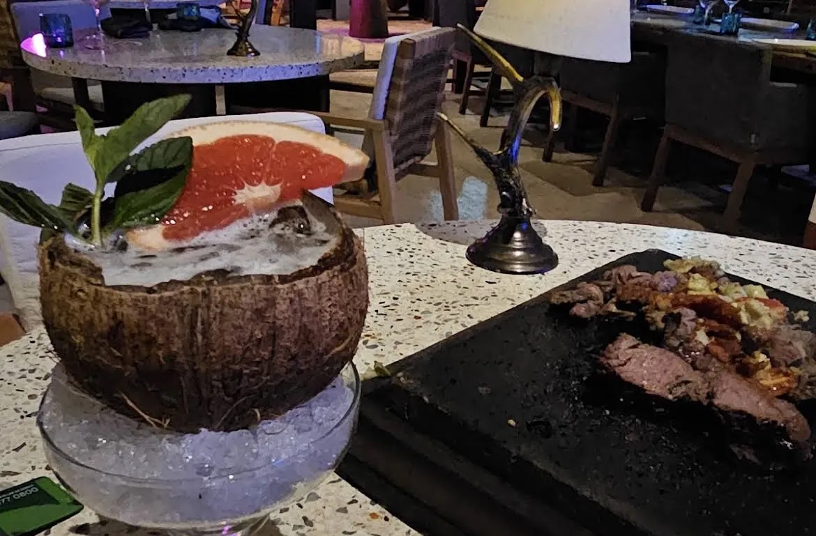 Cocktail served in a coconut next to grilled meat