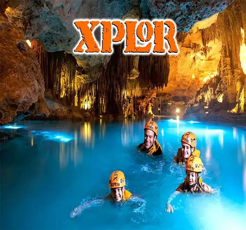Visitors in helmets swimming in an underground river with stalactites